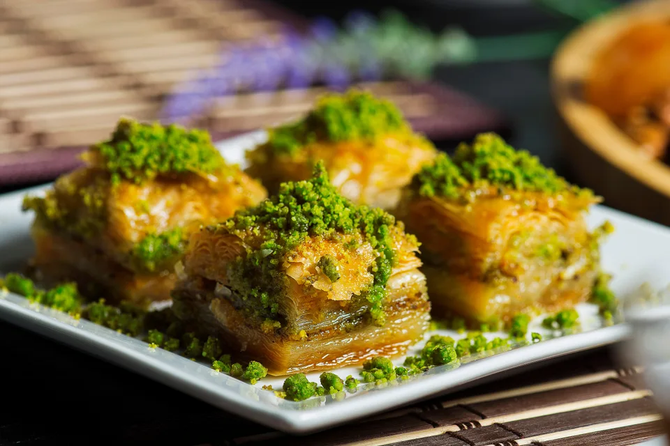 Voorbeeldfoto: Vier stukke laag-baklava met fyngemaakte pistachios bo-op op 'n wit bord