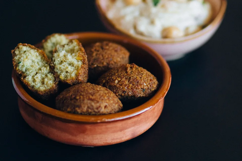 Voorbeeldfoto: Falafelballetjies, insluitend 'n oopgesnyde stuk, in 'n bak met hummus agter
