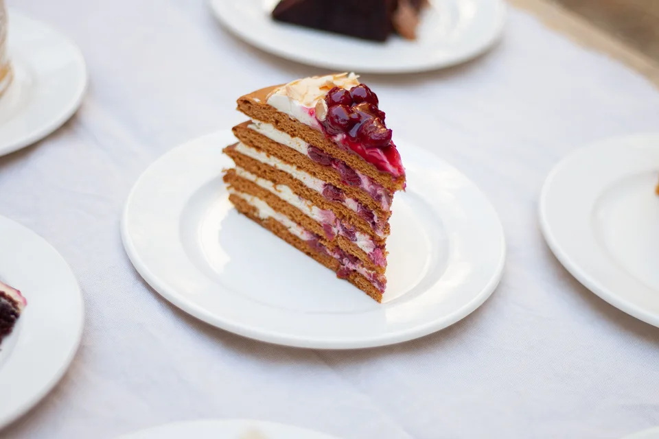 Voorbeeldfoto: 'n Sny laagkoek met bessies bo-op op 'n wit bord