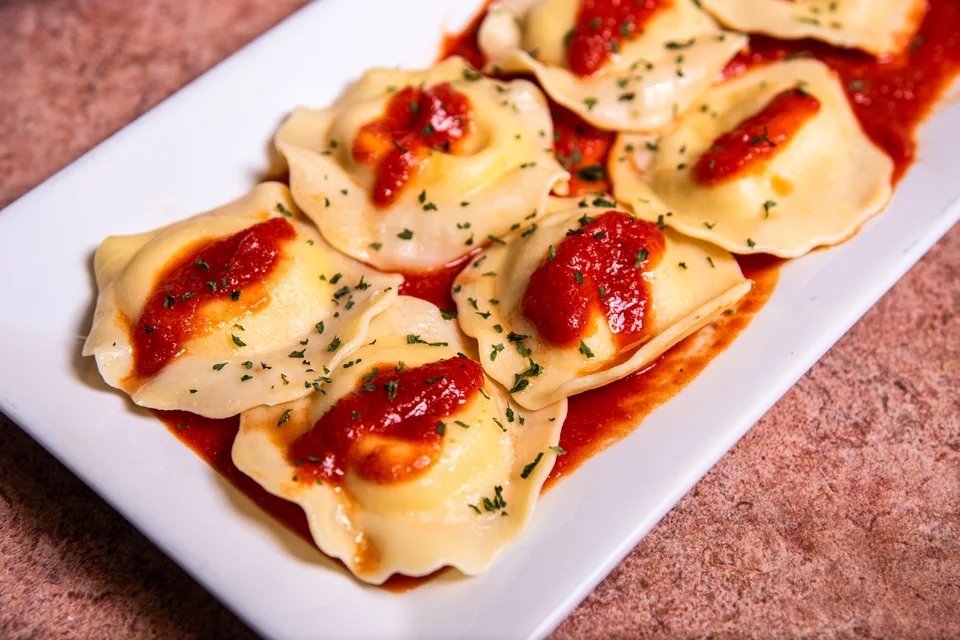 Voorbeeldfoto: Ravioli met tamatiesous en kruie bo-op op 'n wit bord
